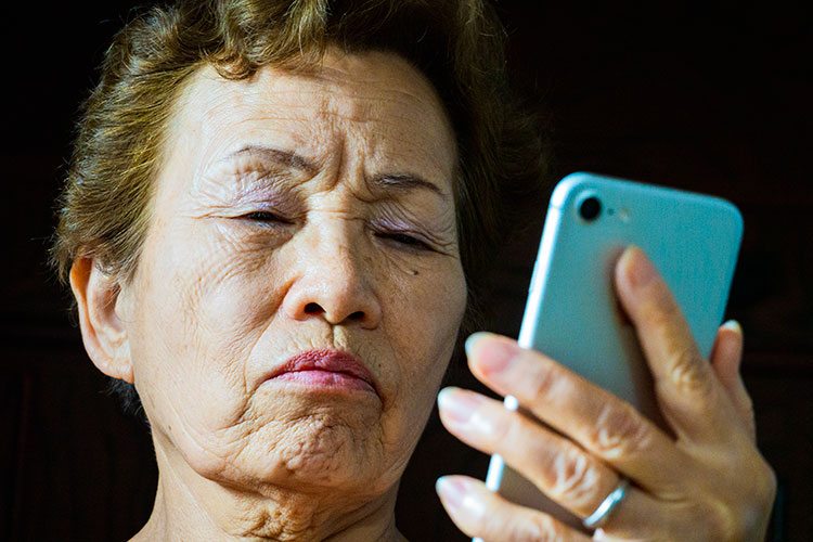 スマートフォンを怪訝そうに見つめる中年女性の写真